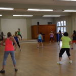A group of Jazzercise students begins to warm up, striding from side to side. 
